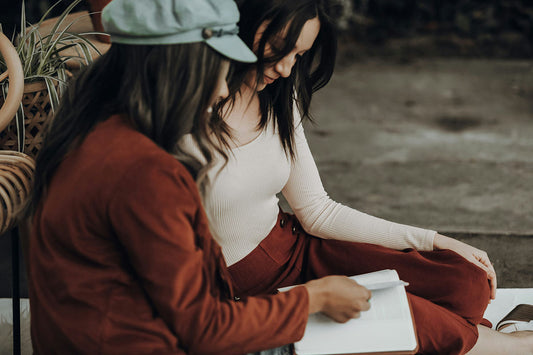 Two women sitting outdoors, reading together