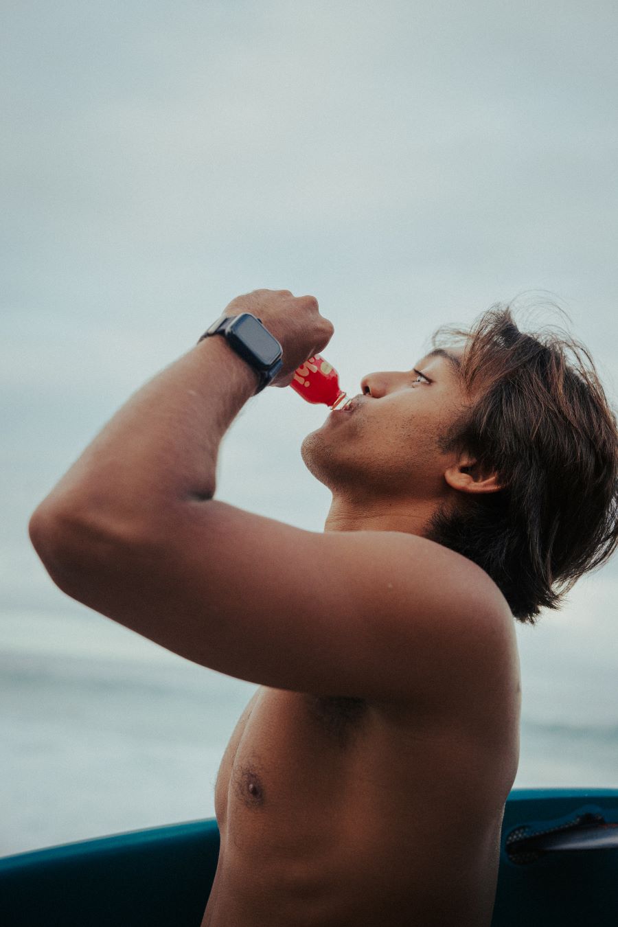 Surfer drinking Jubi energy shot on the beach.